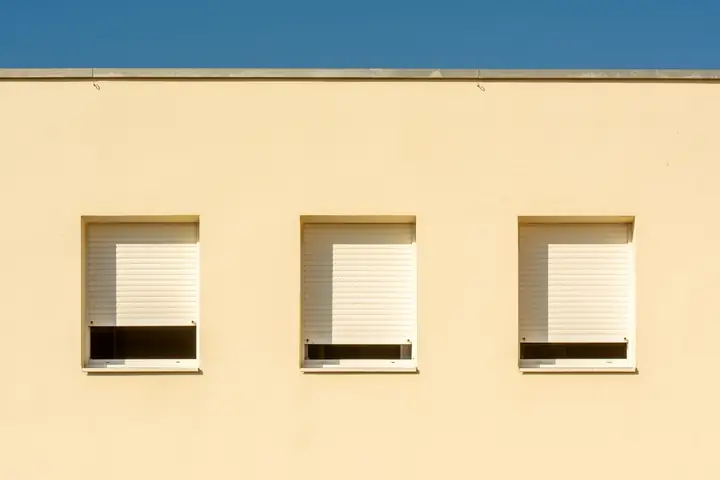 Hausfassade mit drei Fenstern und heruntergelassenen weißen Rollläden