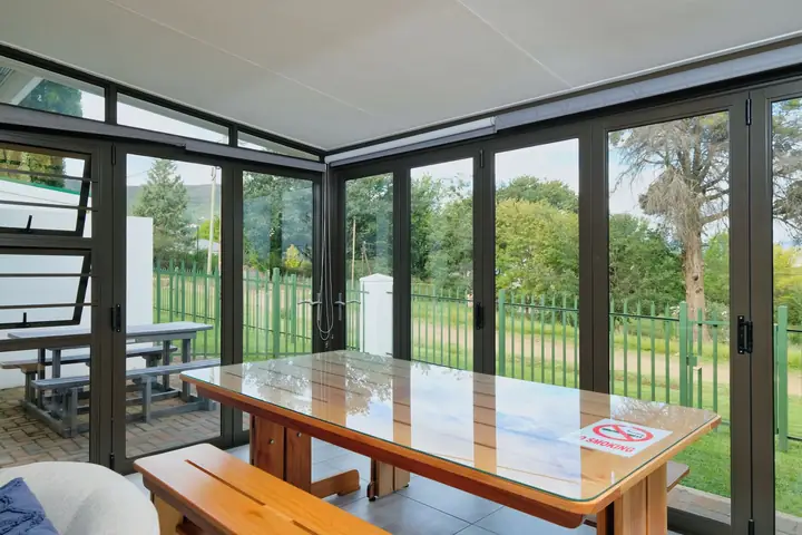 Wintergarten aus Glas mit Holztisch und Blick in einen grünen Garten